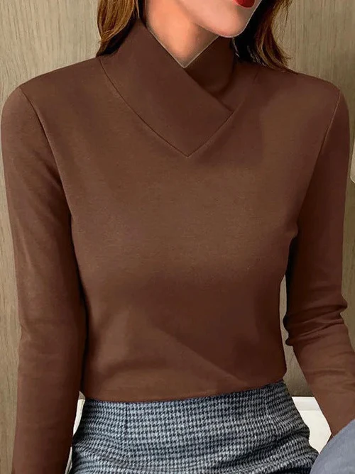 Femme portant un pull marron à col montant et manches longues, associé à une jupe à carreaux gris. Mode élégante et tendance automne-hiver.
