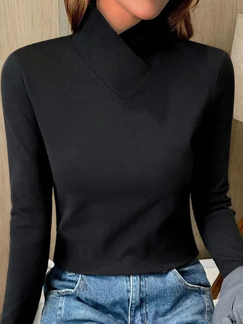 Femme portant un pull noir à col montant croisé, manches longues, associé à un jean bleu décontracté. Mode élégante et moderne.