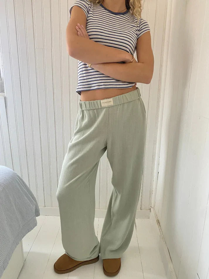 Femme en t-shirt rayé et pantalon ample vert clair, posant dans une chambre minimaliste. Mode décontractée, style confortable, intérieur moderne.
