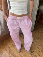 Femme portant un pantalon rose ample à taille élastique, associé à un débardeur blanc, posant sur un sol en bois. Mode décontractée, tendance.