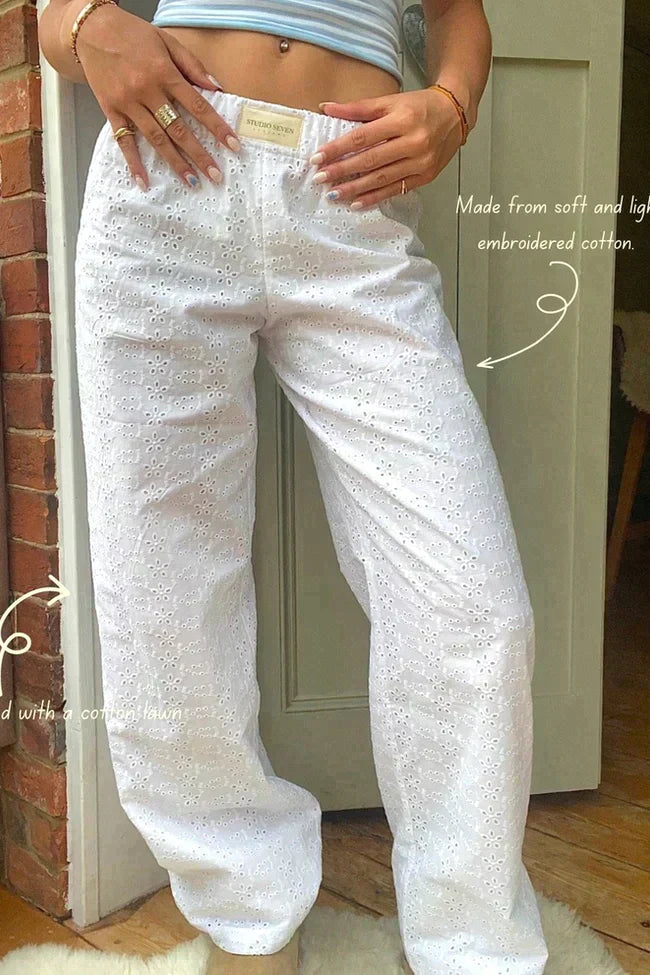 Pantalon blanc en coton brodé, léger et doux, porté par une personne devant une porte en bois. Mode estivale, confort, style décontracté.