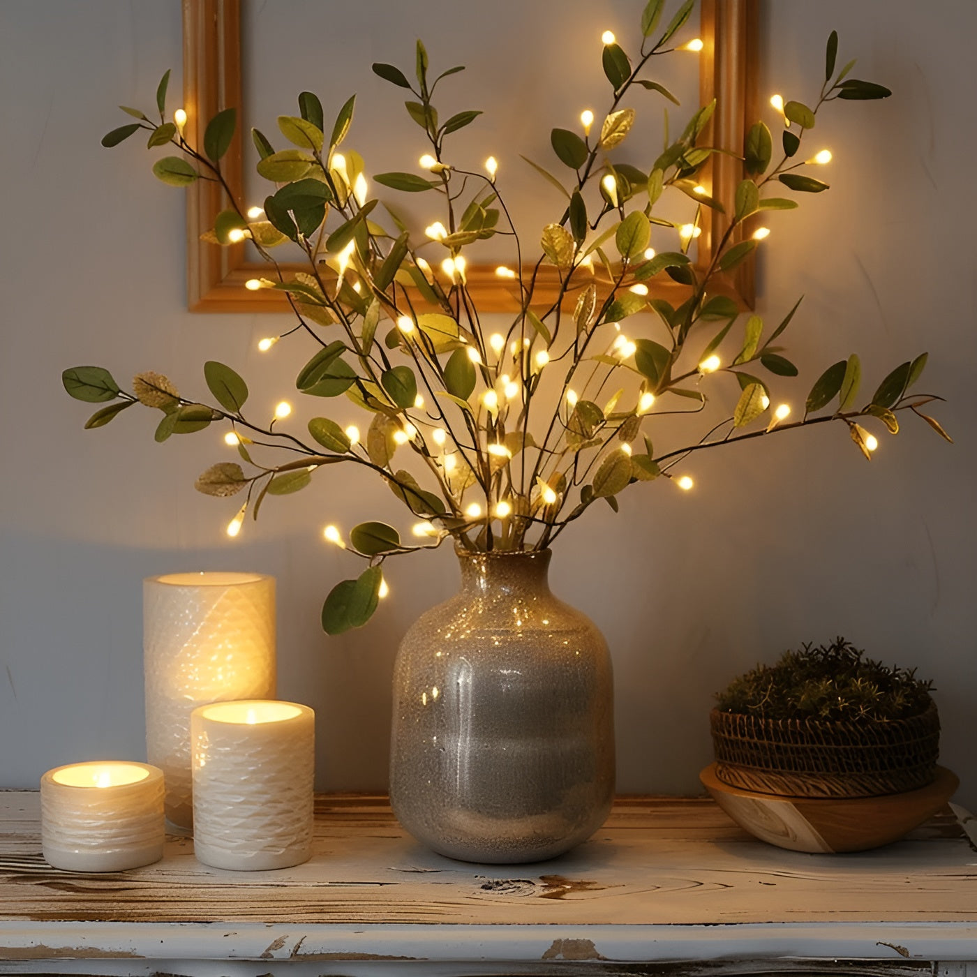 Vase en céramique avec branches lumineuses LED, entouré de bougies blanches allumées sur une table en bois, créant une ambiance chaleureuse et cosy.