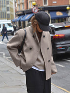 Femme portant un manteau beige élégant, casquette noire, dans une rue urbaine animée. Mode automne, style décontracté chic, tendance urbaine.
