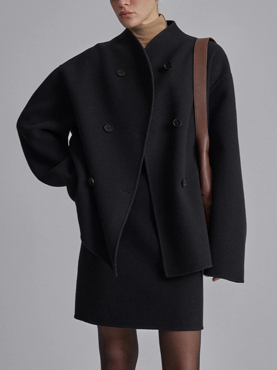 Femme portant un manteau noir oversize à double boutonnage, avec un sac en cuir marron. Mode automne-hiver élégante et moderne.