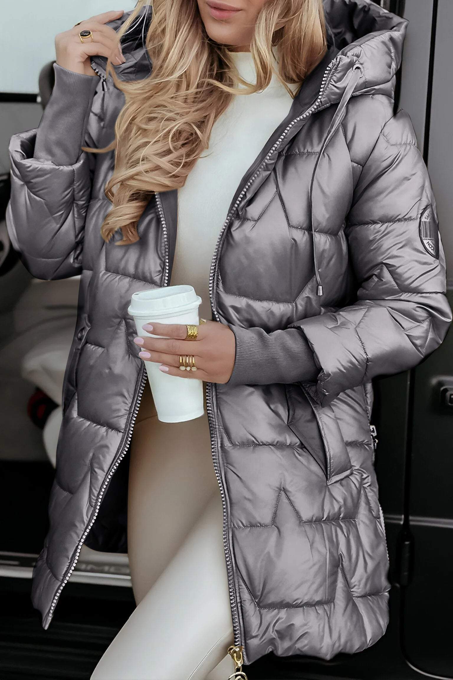 Femme en doudoune argentée, tenant un gobelet de café, devant une voiture. Mode hiver, style chic, tenue décontractée.