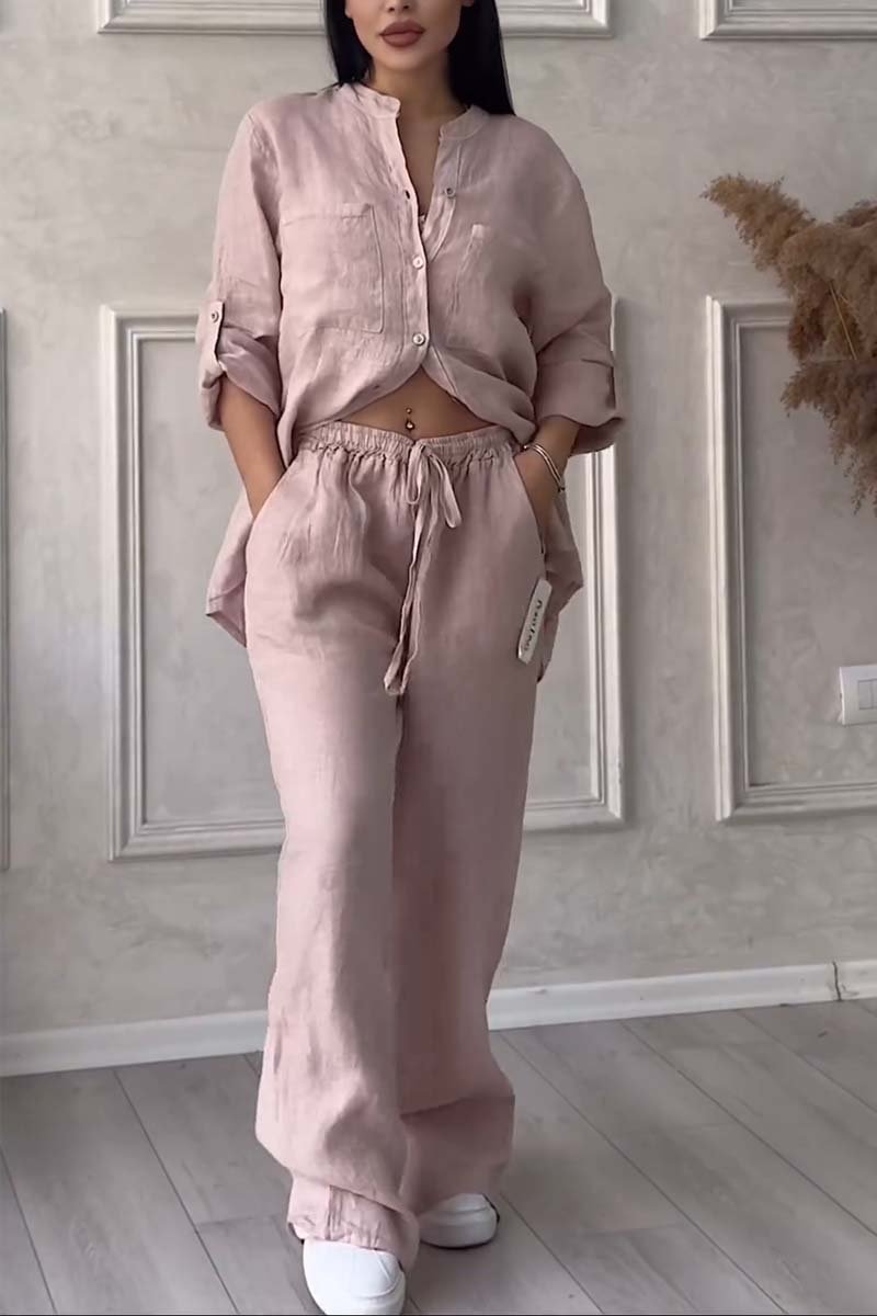 Femme portant un ensemble en lin rose, chemise ample et pantalon à cordon, posant dans un intérieur moderne. Mode décontractée, tendance et élégante.