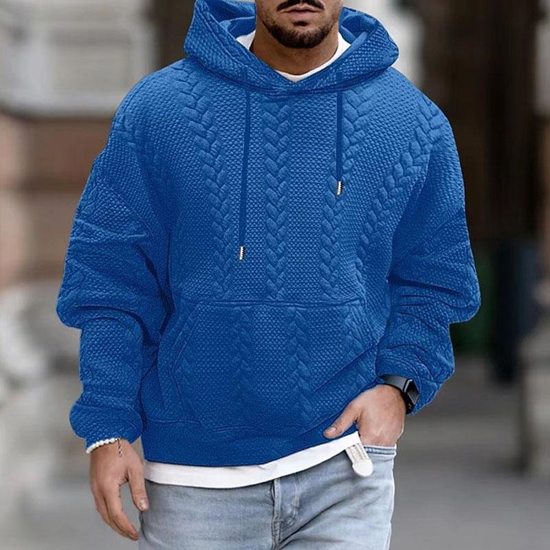 Homme portant un sweat à capuche bleu texturé, style décontracté, mode masculine, rue urbaine. Vêtements tendance automne-hiver.