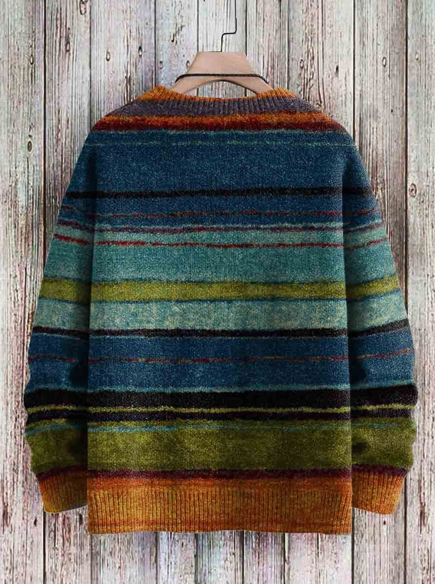 Pull rayé multicolore en laine, tons bleus, verts et marrons, suspendu sur un cintre en bois, fond de planches en bois rustiques.