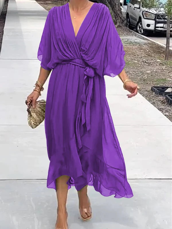 Robe violette élégante en mousseline, manches courtes, ceinture nouée, portée par une femme marchant sur un trottoir. Mode féminine chic et tendance.