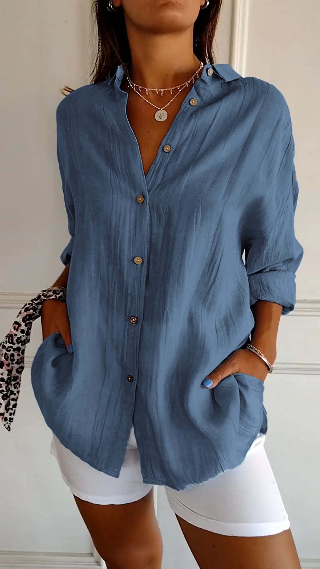 Femme portant une chemise bleue ample à manches longues, boutons en bois, avec un pantalon blanc. Style décontracté, mode féminine élégante.