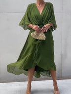 Robe verte élégante avec manches fluides, ceinture à la taille, accessoirisée d'une pochette dorée. Mode féminine chic et tendance.