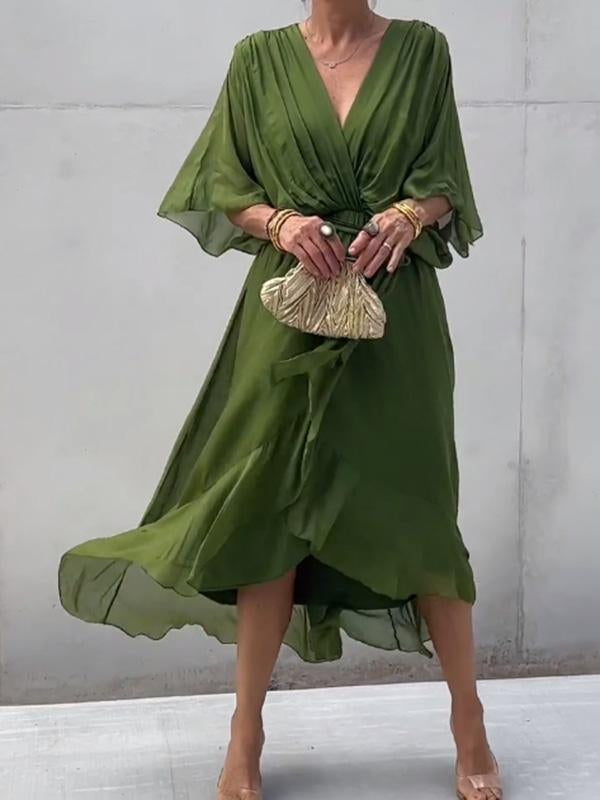 Robe verte élégante avec manches fluides, ceinture à la taille, accessoirisée d'une pochette dorée. Mode féminine chic et tendance.