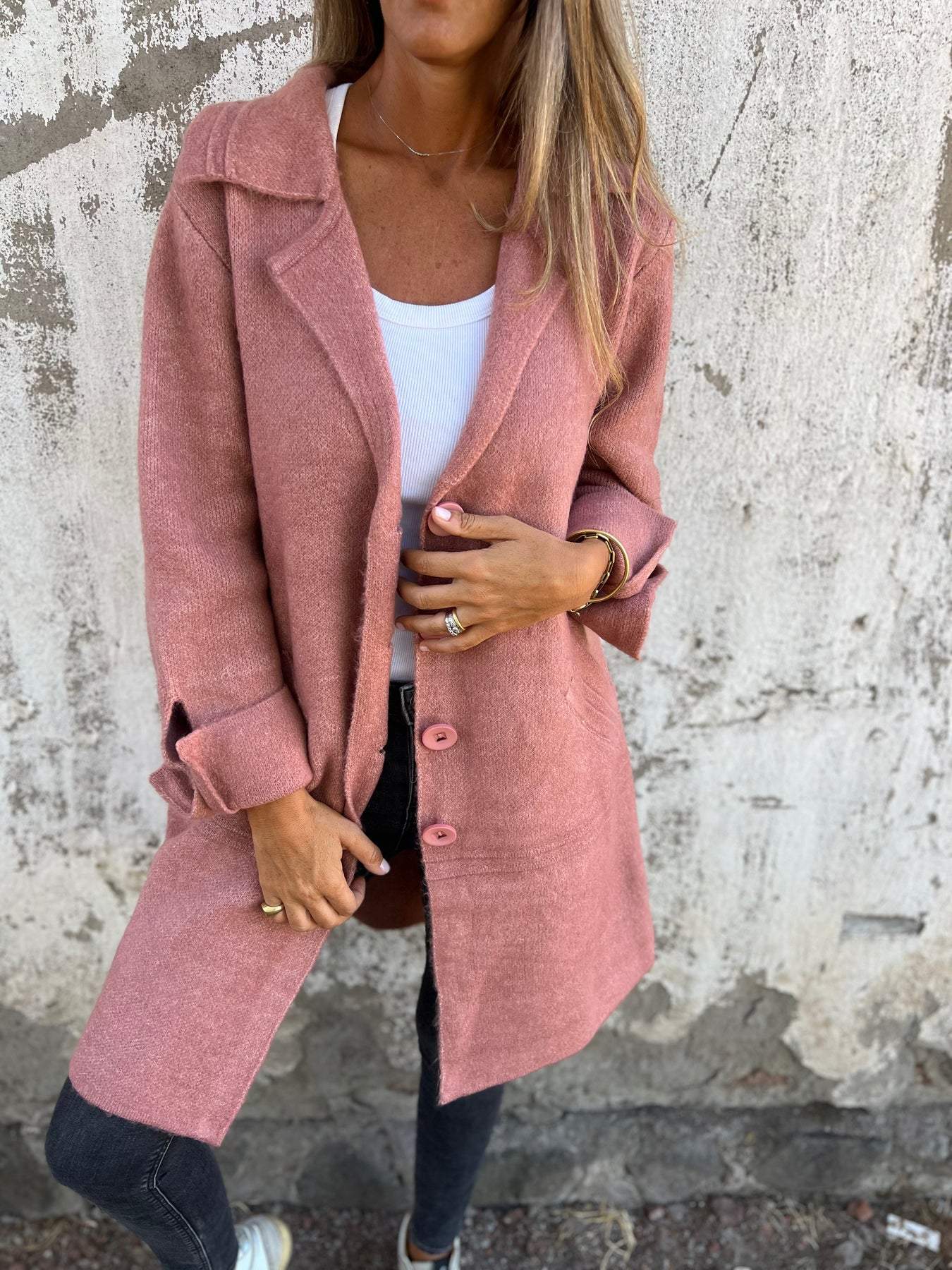 Femme portant un manteau rose élégant, sur fond de mur texturé. Mode automne, style décontracté chic, tendance vestimentaire féminine.