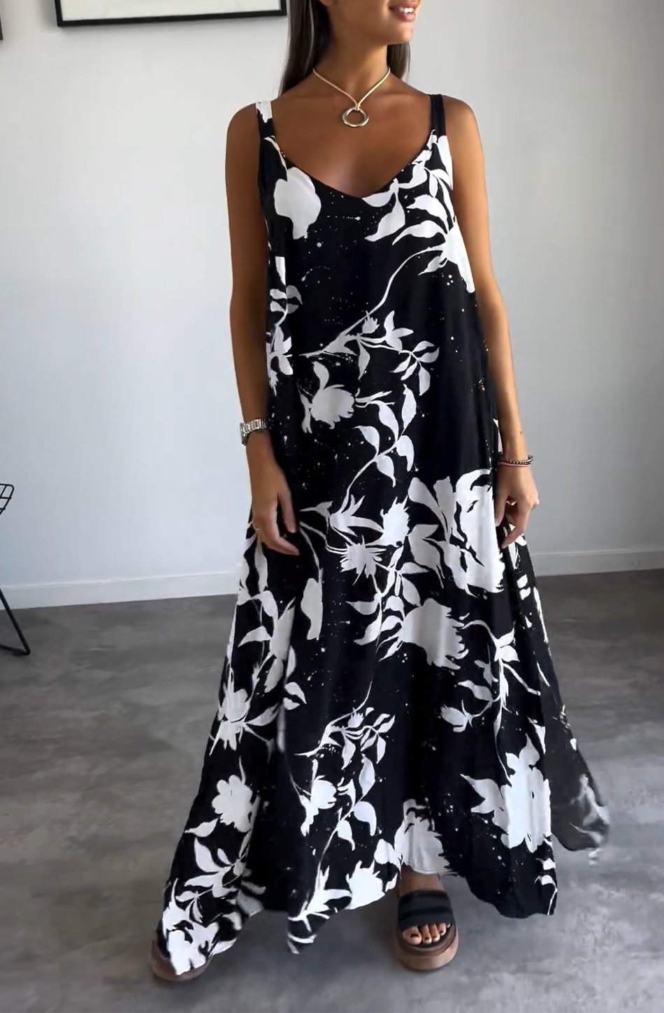 Robe longue noire et blanche à motifs floraux, portée par une femme. Style élégant et décontracté, idéal pour l'été. Accessoires minimalistes.