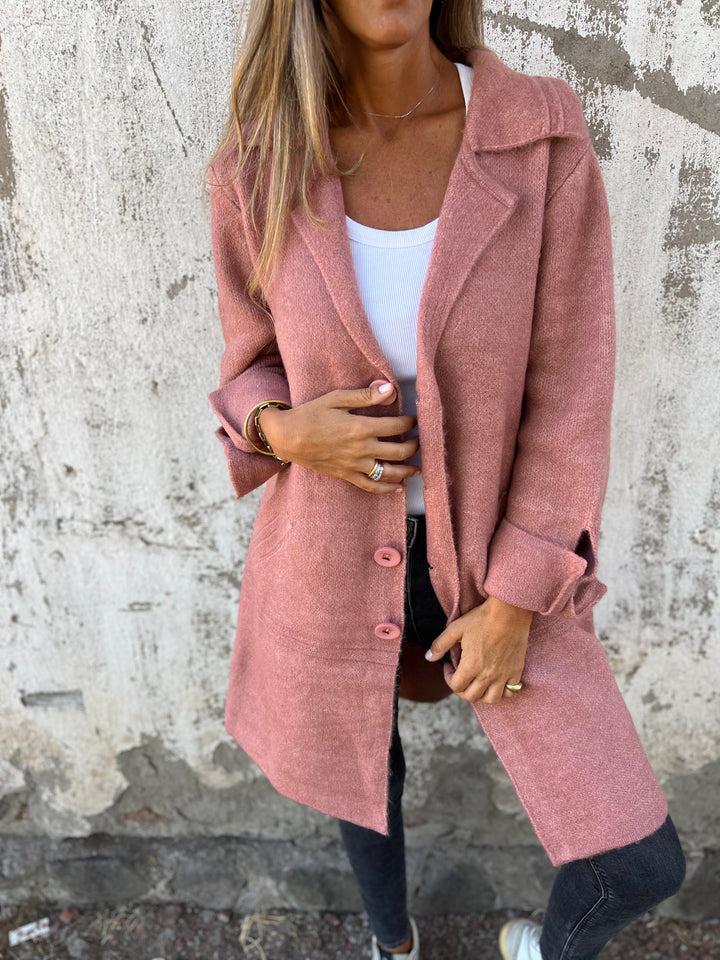 Femme portant un manteau rose élégant, sur fond de mur texturé. Mode automne, style décontracté, tendance féminine, tenue chic.
