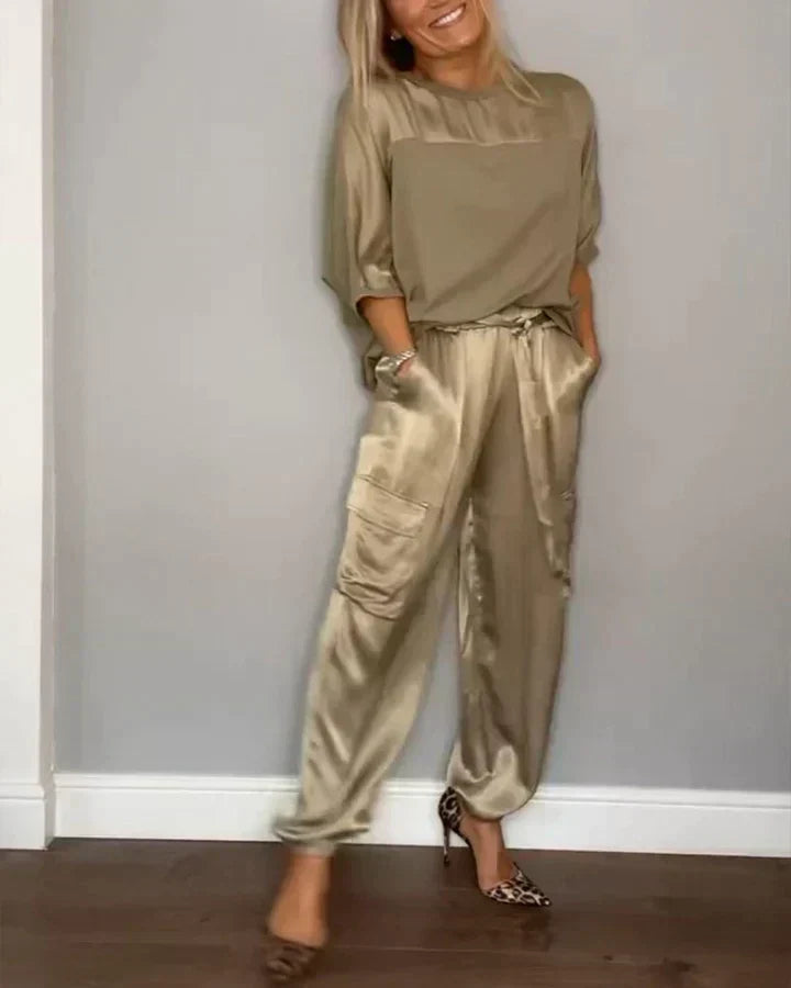 Femme portant une tenue élégante en satin beige, composée d'un haut ample et d'un pantalon cargo, posant contre un mur, chaussures à talons léopard.