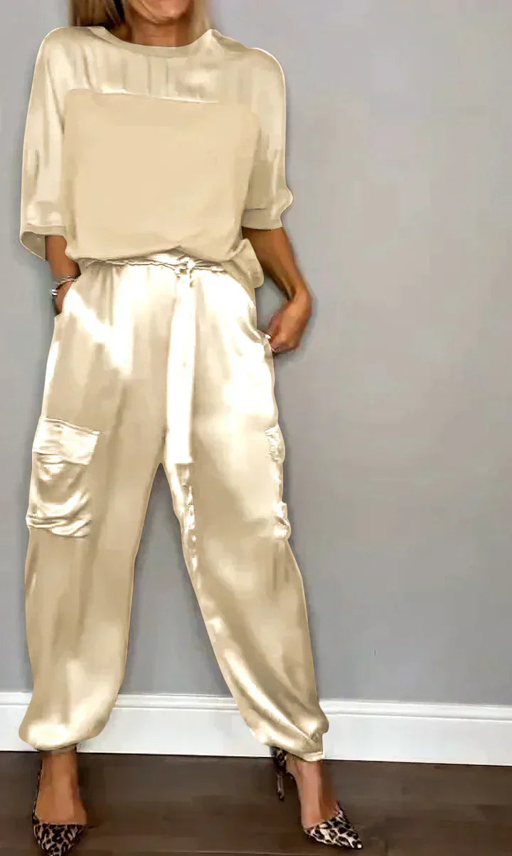 Femme portant un ensemble élégant en satin beige avec un haut ample et un pantalon à poches, chaussures à talons imprimé léopard, sur fond gris.