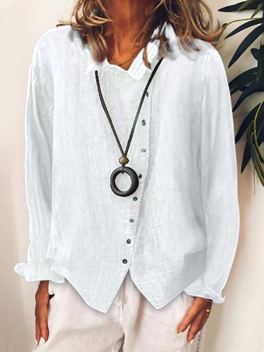 Chemise blanche en lin pour femme avec col en V, manches longues et boutons, accessoirisée d'un collier pendentif rond, style décontracté élégant.