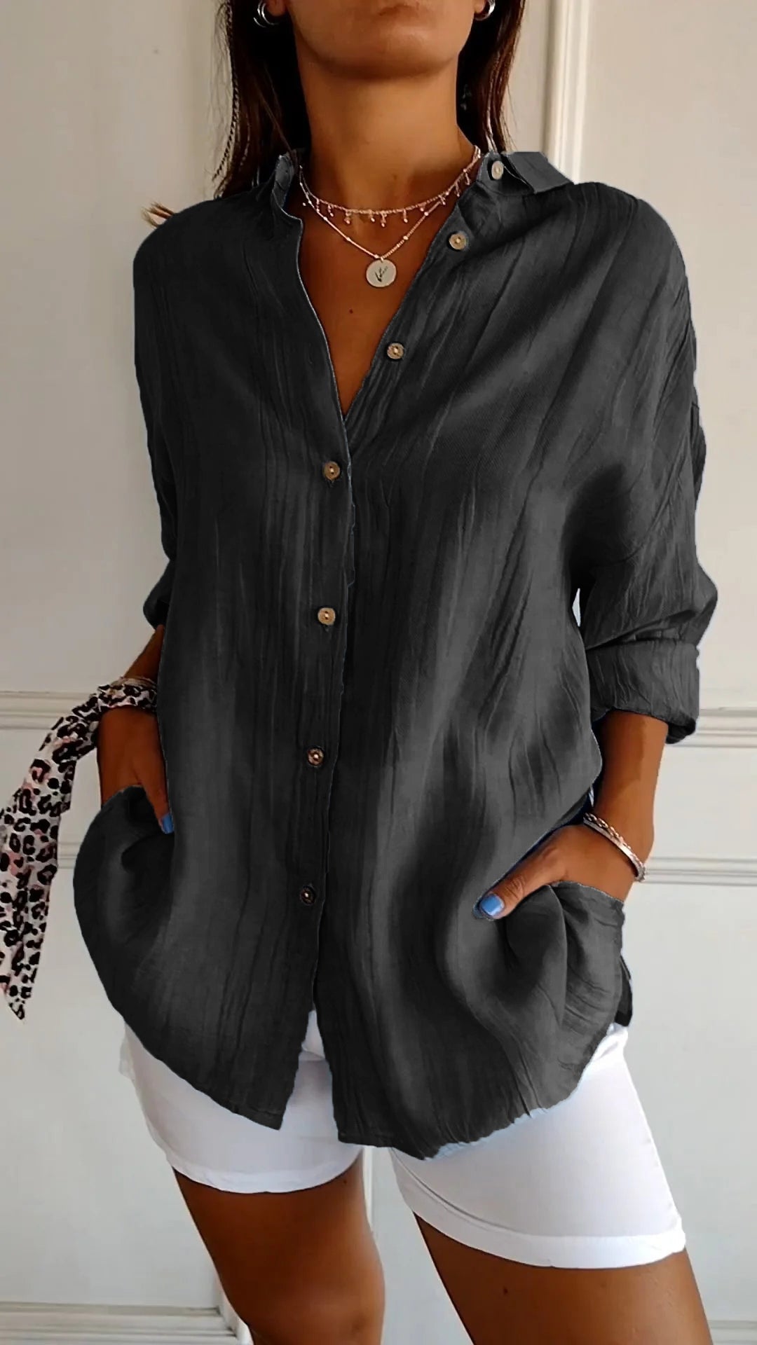 Femme portant une chemise noire ample avec boutons, manches retroussées, col ouvert, associée à un pantalon blanc. Style décontracté et élégant.