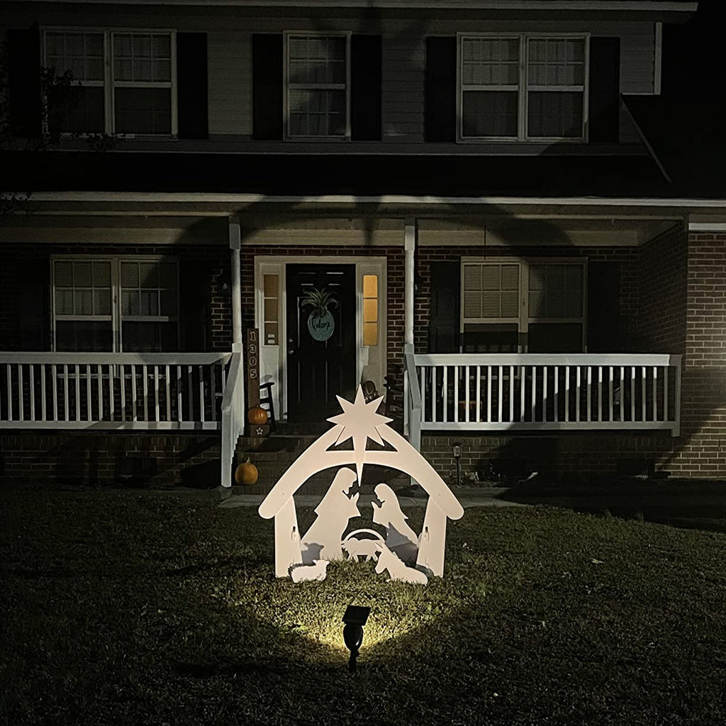 Crèche de Noël illuminée devant une maison en brique, avec personnages en silhouette blanche, étoile au sommet, ambiance festive nocturne.