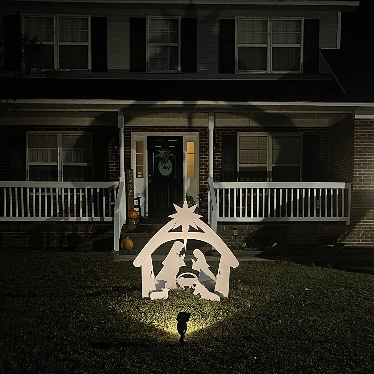 Crèche de Noël illuminée devant une maison en brique, avec personnages en silhouette blanche, étoile au sommet, ambiance festive nocturne.