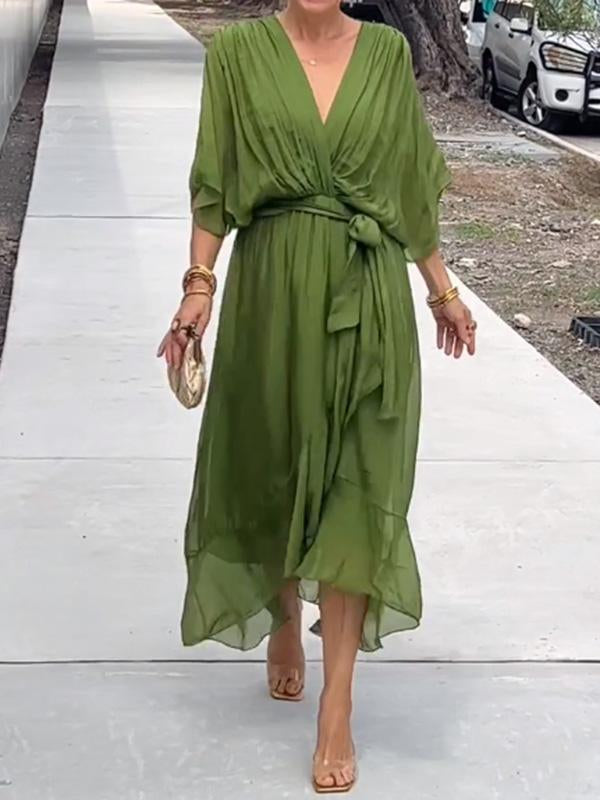 Robe verte élégante en mousseline, ceinturée à la taille, portée par une femme marchant sur un trottoir. Mode féminine chic et estivale.
