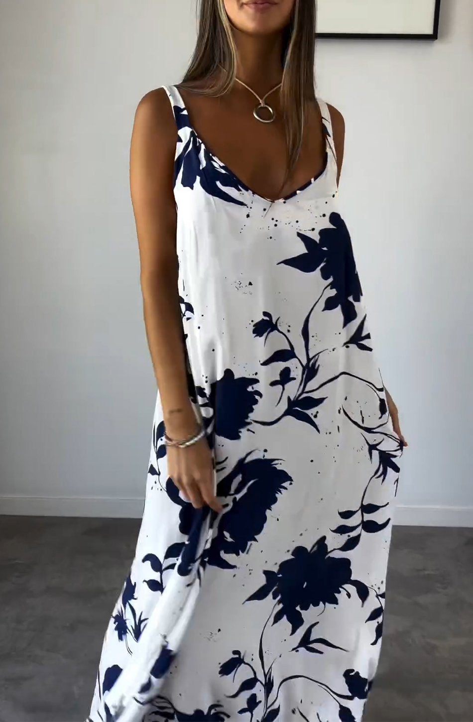Robe longue d'été blanche à motifs floraux bleus, sans manches, col en V, portée par une femme. Mode féminine élégante et décontractée.