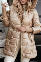 Femme portant une doudoune dorée avec capuche, tenant un gobelet blanc. Mode hiver élégante, manteau matelassé tendance, look chic et moderne.