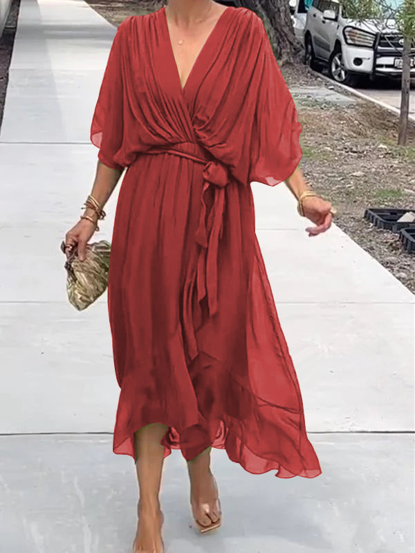 Robe rouge fluide élégante avec manches courtes, ceinture nouée à la taille, portée par une femme marchant sur un trottoir. Mode féminine chic.