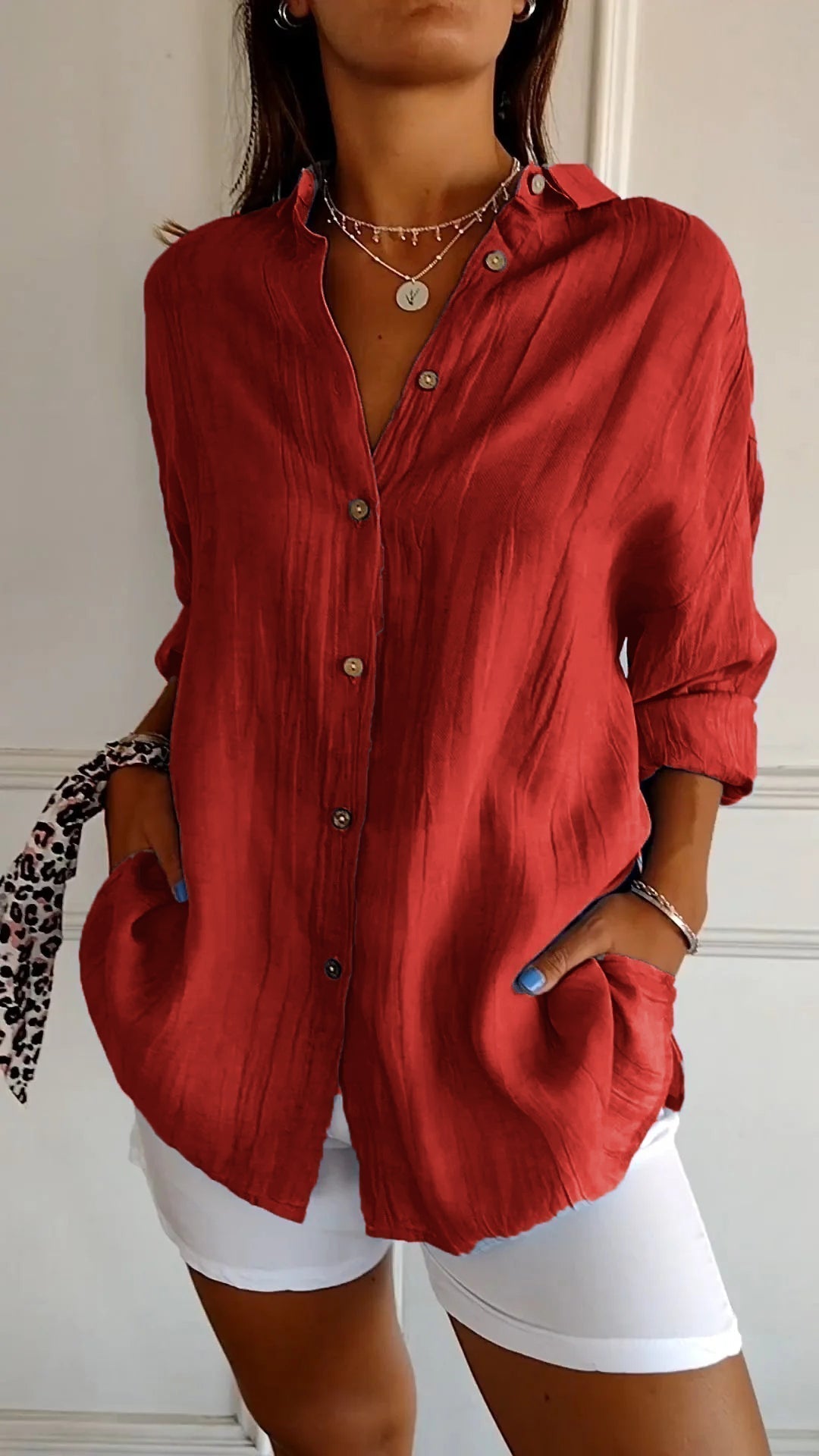Femme portant une chemise rouge ample avec boutons, manches retroussées, col ouvert, associée à un pantalon blanc. Style décontracté et élégant.
