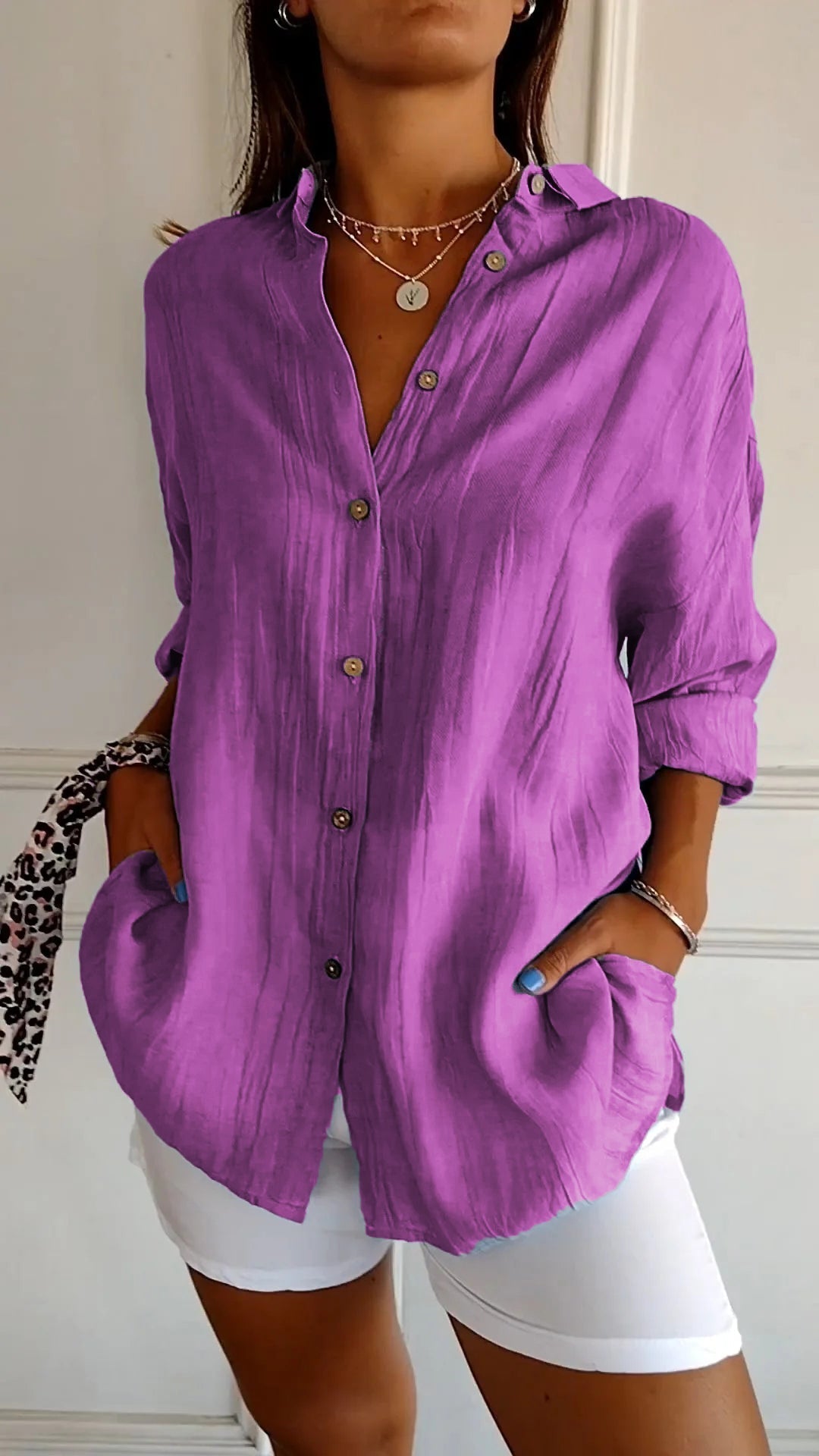 Chemise violette en lin pour femme, manches longues, boutons en bois, poches avant, portée avec un pantalon blanc. Mode féminine élégante.