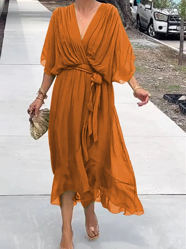 Robe orange fluide avec ceinture nouée, manches courtes, portée par une femme marchant sur un trottoir. Mode estivale élégante et décontractée.