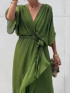 Robe verte élégante avec manches amples et ceinture nouée, tenue chic pour femme, accessoirisée de bracelets dorés et pochette zébrée.
