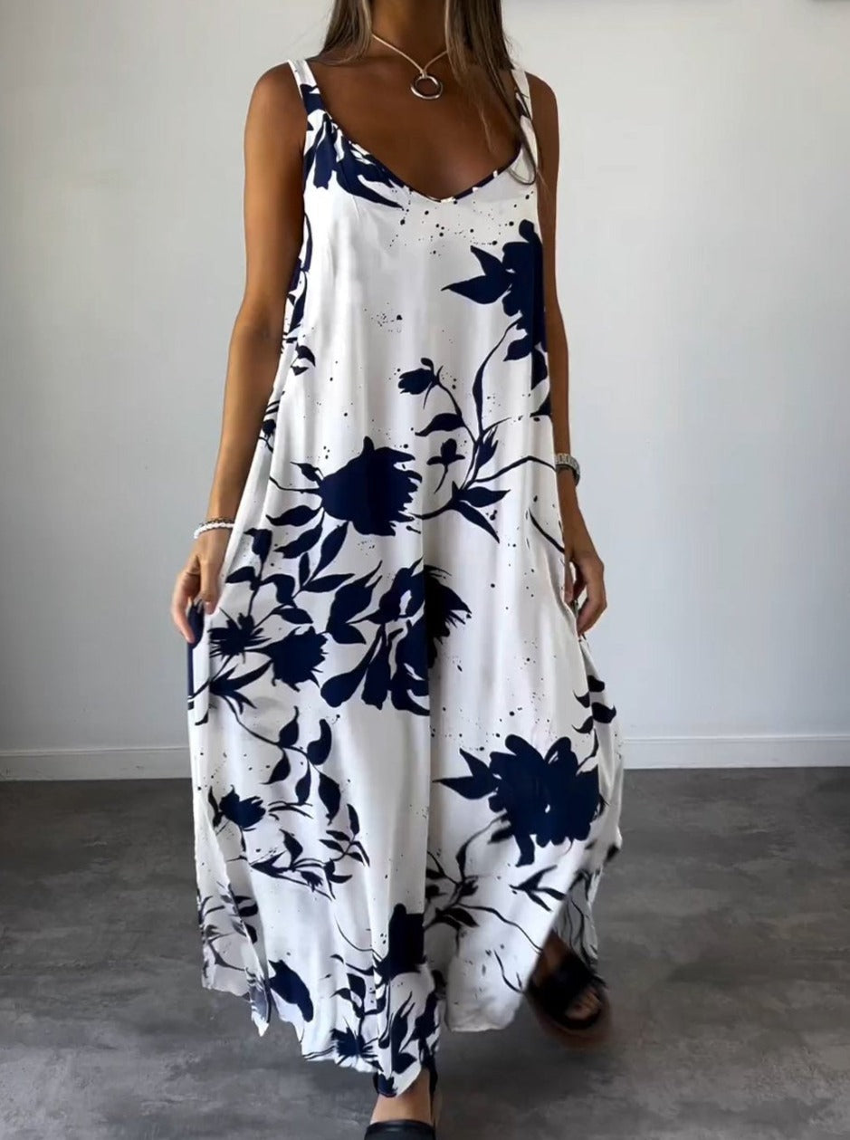 Robe longue blanche à motifs floraux bleus, sans manches, portée par une femme. Style décontracté, idéal pour l'été. Mode féminine élégante.