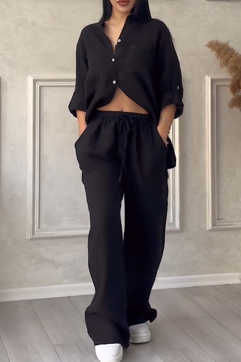 Femme portant un ensemble noir décontracté, chemise et pantalon ample, posant dans un intérieur moderne. Mode féminine, tenue confortable, style chic.