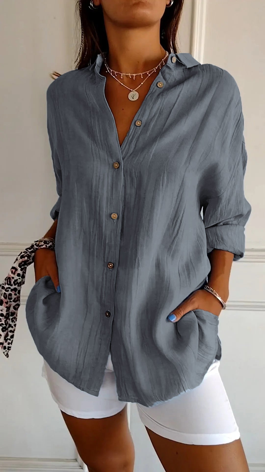 Femme portant une chemise grise ample avec boutons, manches retroussées, et un pantalon blanc. Style décontracté, mode féminine élégante.