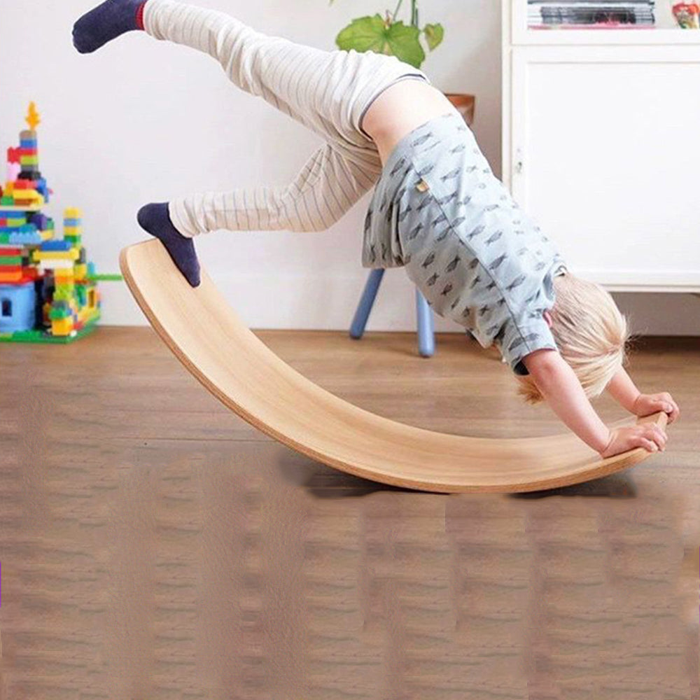 Enfant jouant sur une planche d'équilibre en bois dans un salon, jouets colorés en arrière-plan. Activité ludique, développement moteur enfant.