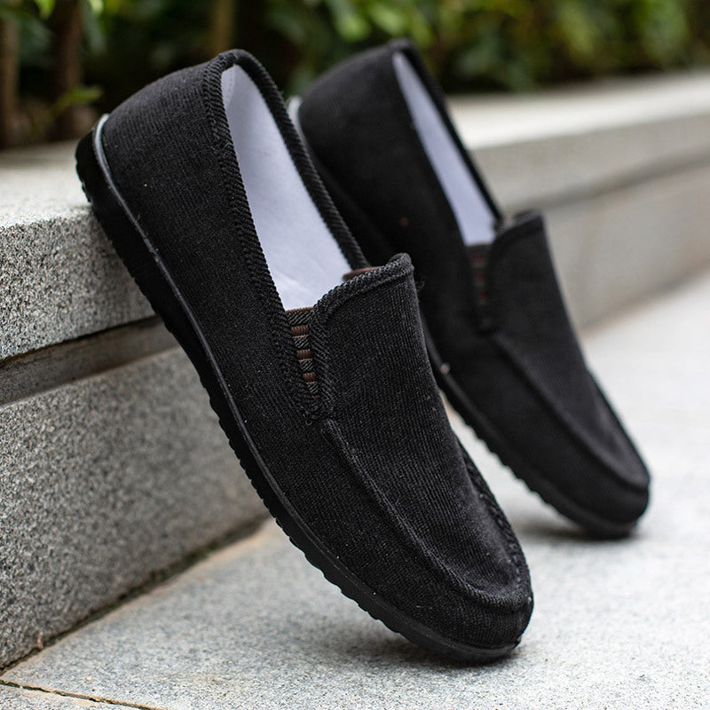Mocassins noirs en toile pour homme posés sur un trottoir en pierre, chaussures décontractées élégantes, idéales pour un style urbain et moderne.