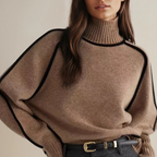 Femme portant un pull en laine beige à col roulé, manches longues, détails noirs, ceinture en cuir noir; mode automne-hiver élégante et chic.