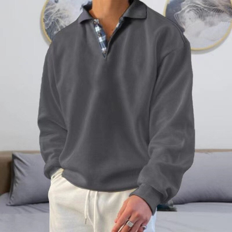 Homme portant un pull gris à col polo sur une chemise à carreaux, pantalon blanc, dans un salon moderne. Mode décontractée, style élégant.