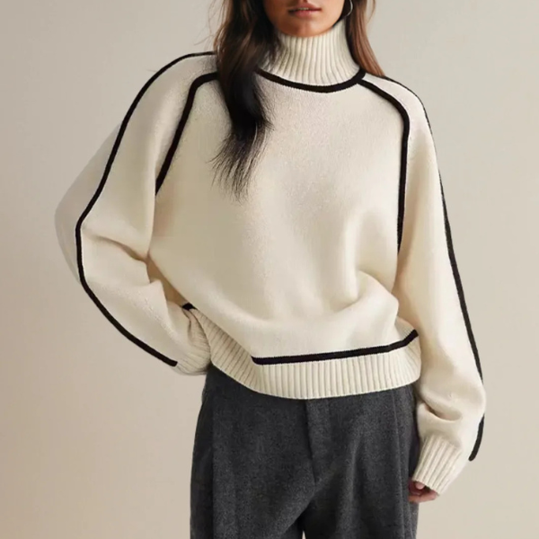 Femme portant un pull blanc à col roulé avec bordures noires, manches longues, associé à un pantalon gris. Mode automne-hiver élégante et moderne.