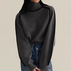 Femme portant un pull en laine gris à col roulé avec des manches longues, associé à un jean bleu. Mode automne-hiver, style décontracté et élégant.