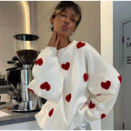 Femme portant un pull blanc à motifs cœurs rouges, posant devant une machine à café moderne. Mode tendance, style décontracté, café.