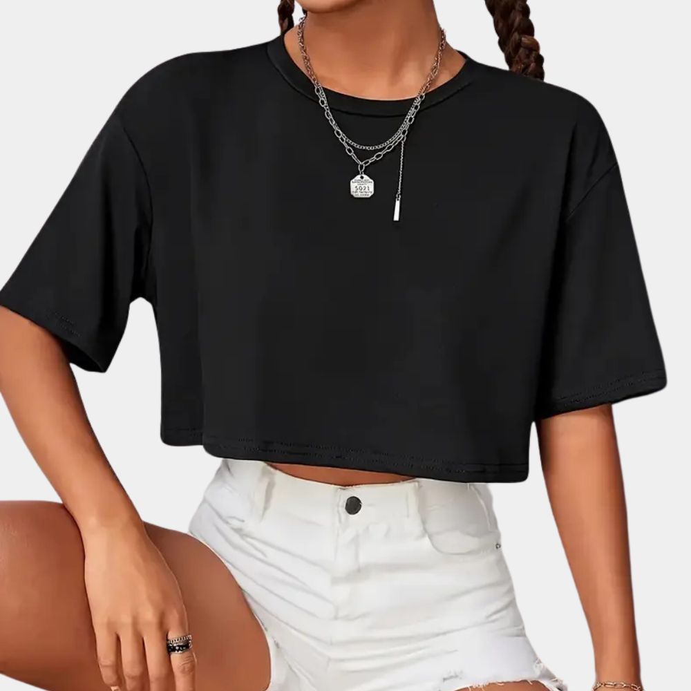 Femme portant un t-shirt noir court et un short blanc déchiré, accessoirisée de colliers en argent. Mode décontractée, tendance été.