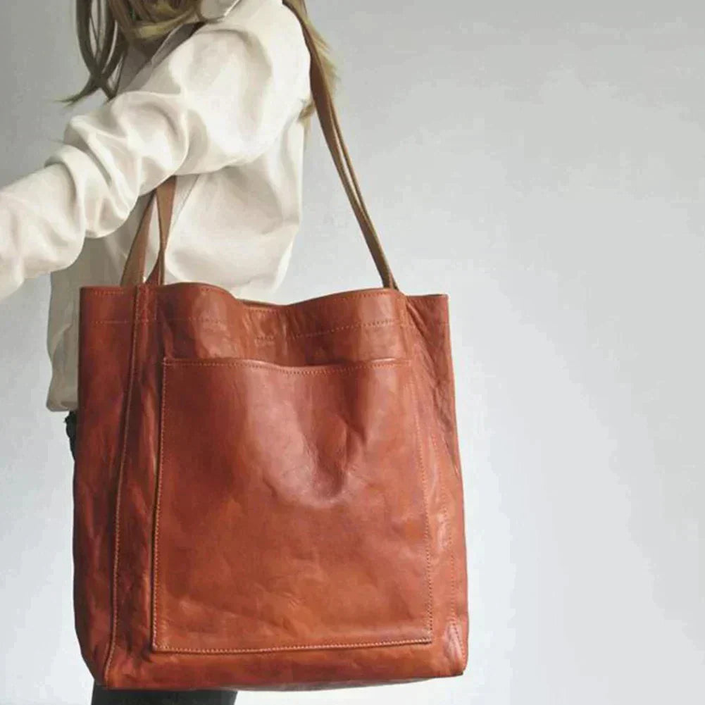 Sac en cuir marron porté à l'épaule, design minimaliste, grande poche avant, idéal pour mode femme, accessoires tendance, style élégant.