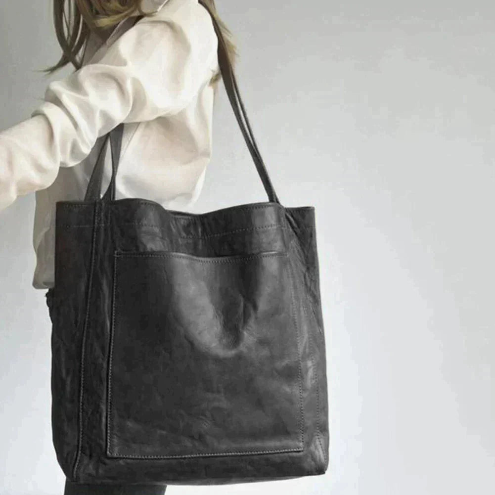 Sac cabas en cuir noir porté par une femme en chemise blanche, design élégant et moderne, accessoire mode tendance pour toutes occasions.