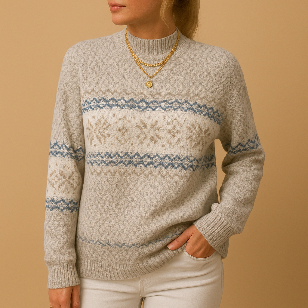 Femme portant un pull en laine à motifs nordiques beige et bleu, col montant, avec colliers dorés, sur fond beige. Mode hiver élégante et confortable.