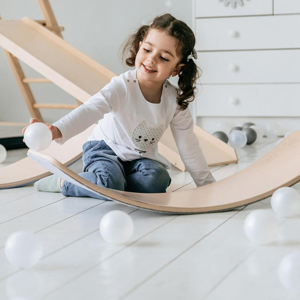 Petite fille jouant avec des balles blanches sur une planche d'équilibre en bois dans une chambre d'enfant lumineuse. Jouet éducatif, motricité.
