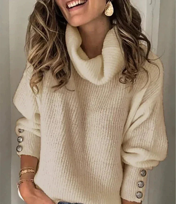 Femme souriante portant un pull en laine blanc à col roulé, manches boutonnées, cheveux ondulés, boucles d'oreilles dorées. Mode automne-hiver tendance.