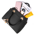 Sac à main noir en cuir avec motifs tressés, contenant tablette, portefeuille rose, maquillage et crème solaire. Accessoire mode femme élégant.